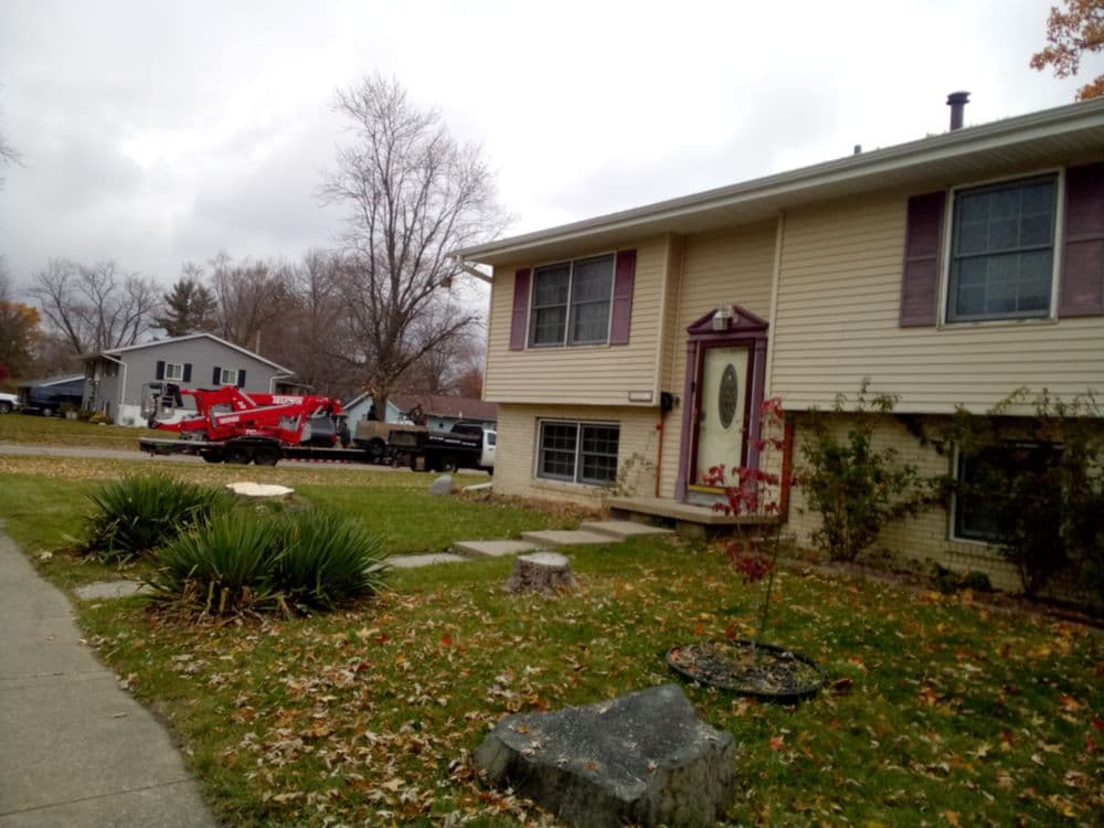 Street view of a two-story house with a front yard and construction equipment nearby.