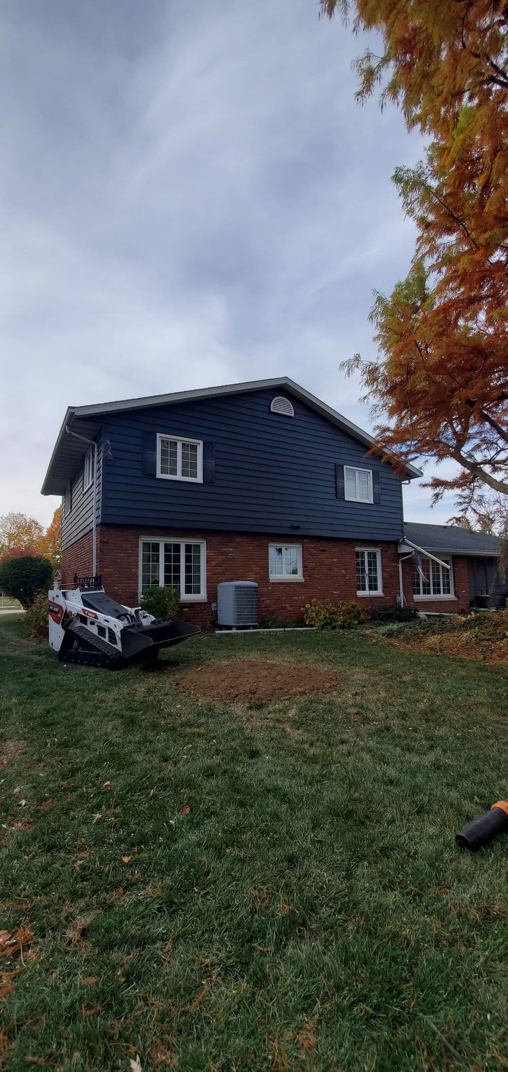 Two-story blue house with brick accents and autumn leaves in the foreground.