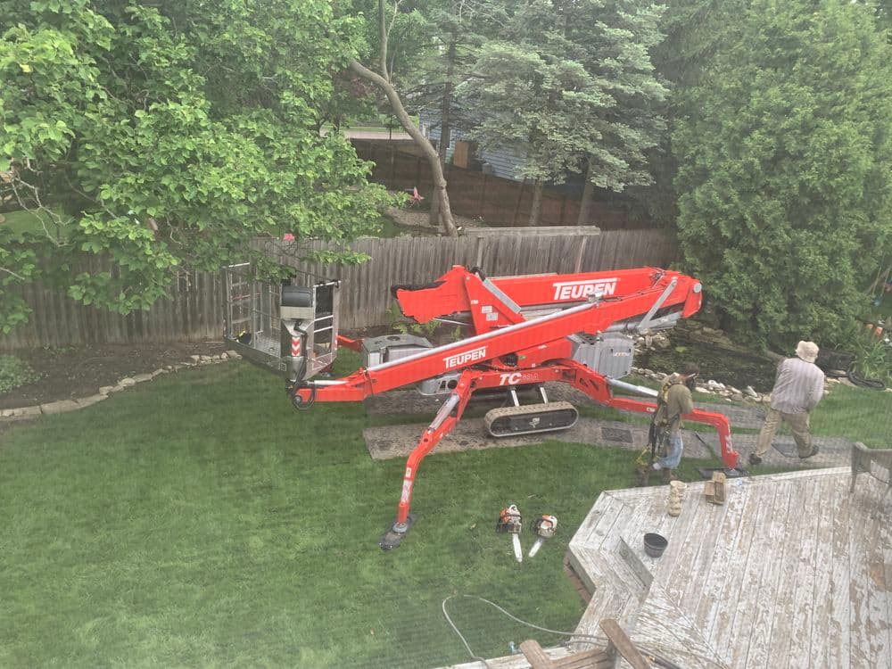 Teurer lift in backyard with workers preparing for maintenance and lush greenery surrounding.