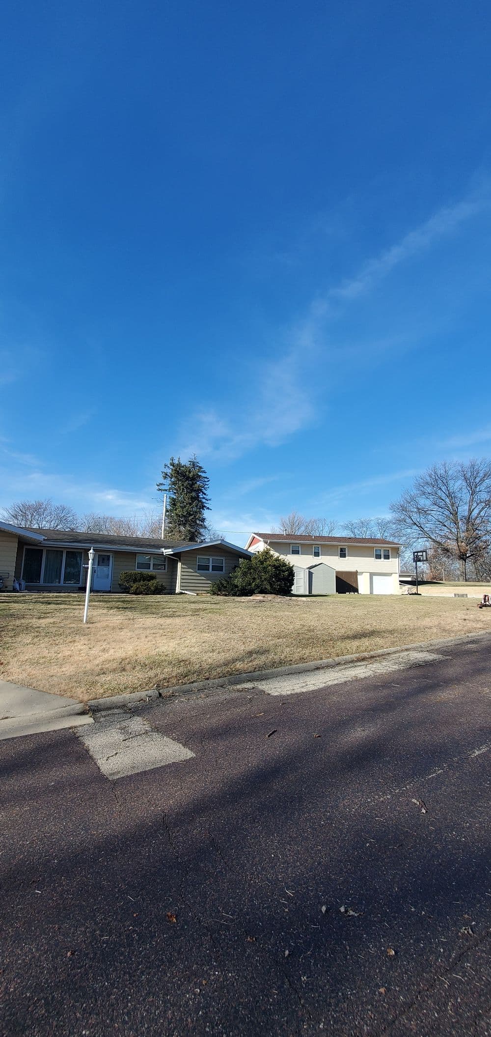 Single-story house with a front lawn under a clear blue sky, featuring a tree and a driveway.