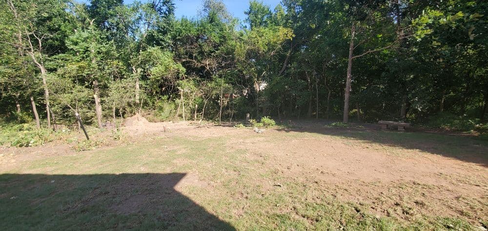 Cleared backyard with fresh soil and trees in the background, ideal for landscaping.