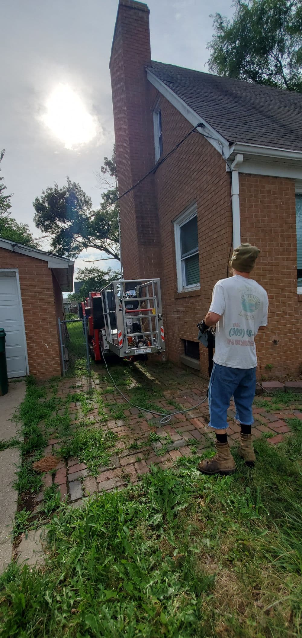 Man operating equipment near a brick house with a truck parked in the driveway.