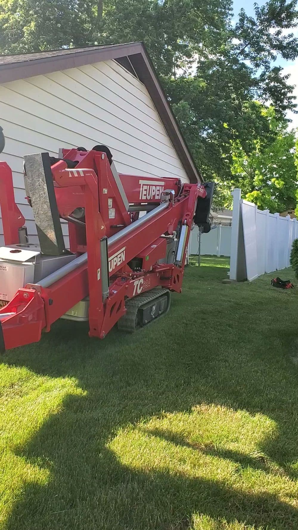 Teupen tracked aerial lift positioned on green grass beside a house and fence.