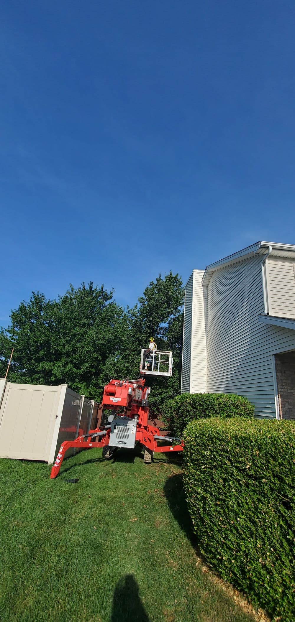 Worker using a lift for maintenance on the side of a house under a clear blue sky.