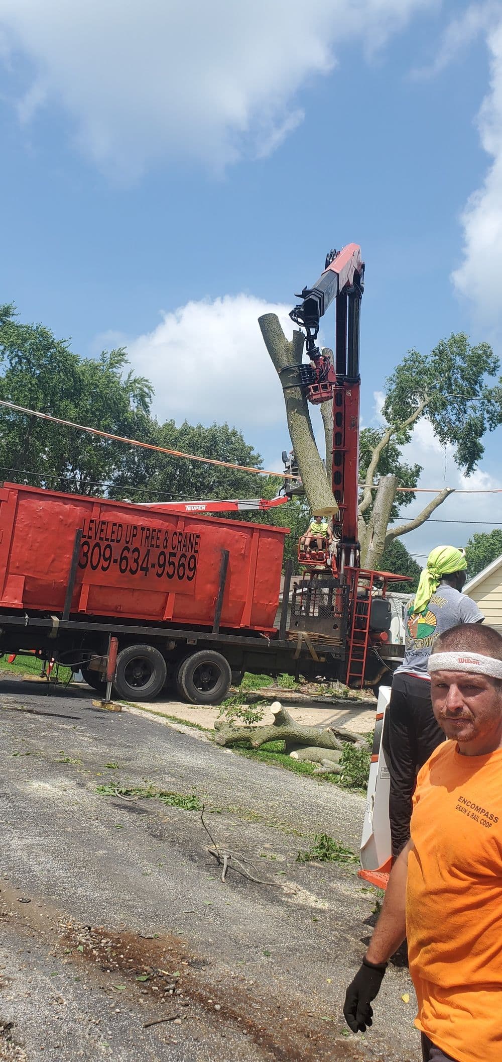 Tree removal using a crane with crew member and truck at residential site.