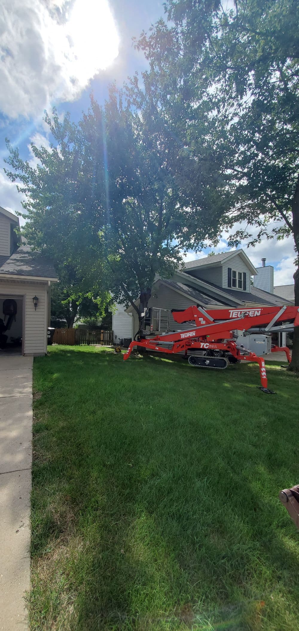 Orange telescopic lift parked on green lawn beside a house under a clear blue sky.