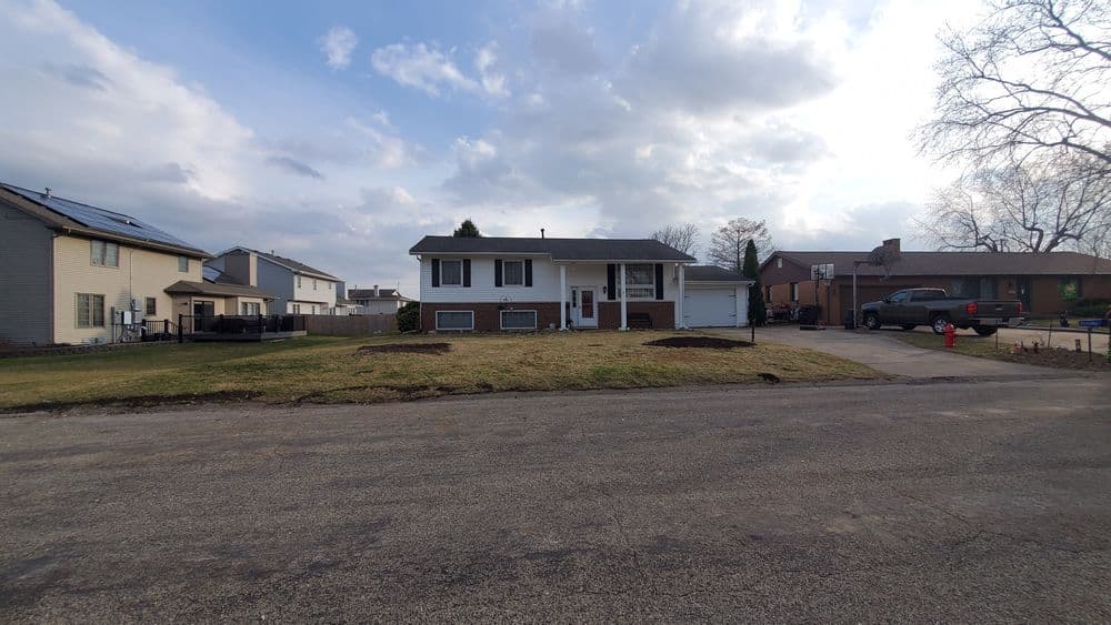 Single-story house with a front lawn, located on a residential street under a cloudy sky.